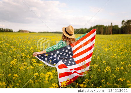 Young woman with american flag on blooming meadow. Independence Day. USA flag fluttering in the wind 124313631