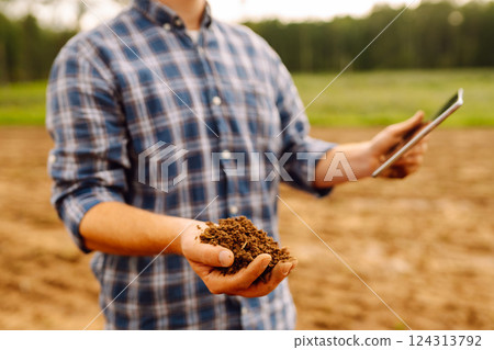 Farmer in a sunny field collects soil, checks its health using a digital tablet. Technology concept 124313792