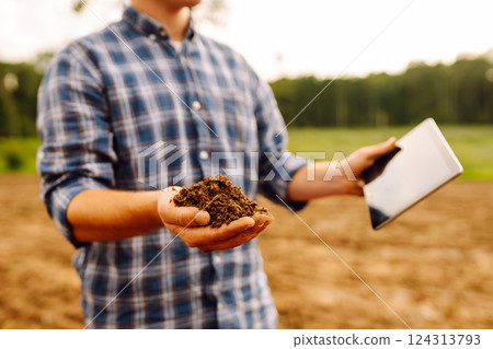 Farmer in a sunny field collects soil, checks its health using a digital tablet. Technology concept Farmer in a sunny field collects soil, checks its health using a digital tablet. Technology concept 124313793
