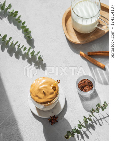 Korean whipped drink Dalgona coffee on a light background with cinnamon and morning shadow. Korean whipped drink Dalgona coffee on a light background with cinnamon and morning shadow. 124314137
