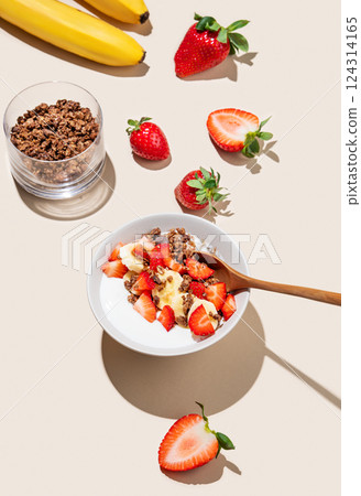 Greek yogurt with chocolate granola, strawberries and banana in a bowl on a beige background 124314165