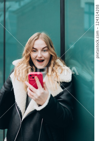 Smiling woman using mobile phone app, playing game, shopping online outdoors. Happy woman celebrating victory in lottery. Amazed hipster wondered with win in online auction betting on website Smiling woman using mobile phone app, playing game, shopping online outdoors. Happy woman celebrating victory in lottery. Amazed hipster wondered with win in online auction betting on website 124314208