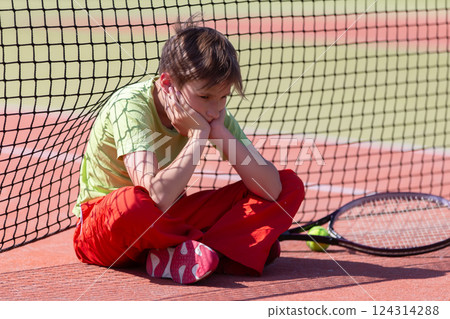 The boy lost the tennis competition. The child sits at the net with a racket. Psychology of sports in childhood. The boy lost the tennis competition. The child sits at the net with a racket. Psychology of sports in childhood. 124314288