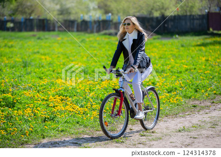 An adult woman rides a bicycle through a spring meadow of dandelions. 124314378