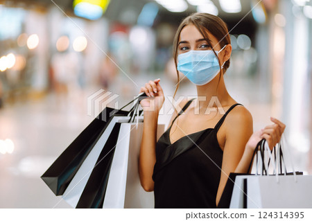 Fashionable woman in protective medical mask with shopping bags walking in the mall. Covid-19. Fashionable woman in protective medical mask with shopping bags walking in the mall. Covid-19. 124314395