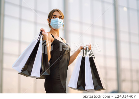 Beautiful woman in protective sterile medical mask with shopping bags near shopping center.Covid- 2019. 124314407