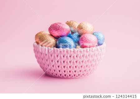 Chocolate easter eggs wrapped in multi colored foil in bowl on pink background. 124314415