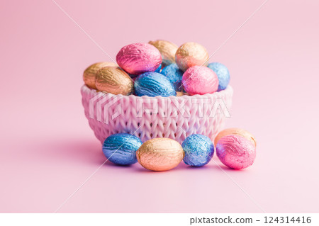 Chocolate easter eggs wrapped in multi colored foil in bowl on pink background. Chocolate easter eggs wrapped in multi colored foil in bowl on pink background. 124314416