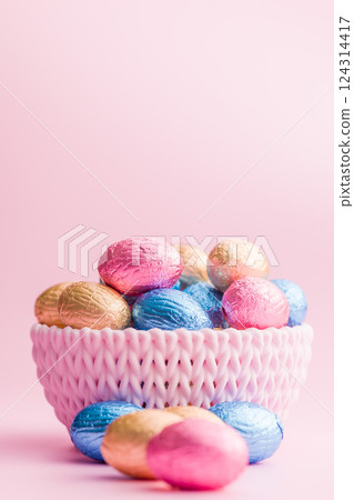 Chocolate easter eggs wrapped in multi colored foil in bowl on pink background. Chocolate easter eggs wrapped in multi colored foil in bowl on pink background. 124314417