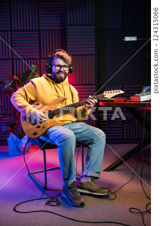 Male singer playing guitar and singing a song. Man performing in a recording studio. Recording music album. 124315066