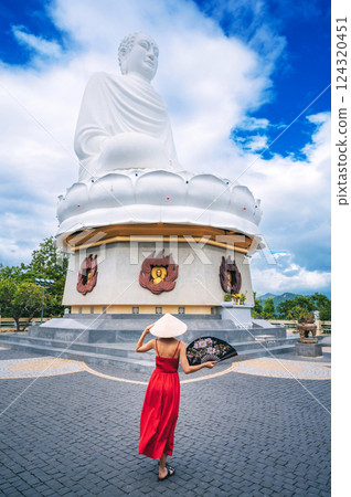 back of woman tourist in Vietnamese hat with fan at Buddha statue at Long Son Pagoda in Nha Trang in Vietnam. Tourism and travel in Asia 124320451