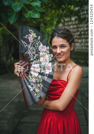 beautiful happy young woman in red dress with fan in the garden. Tourism and travel in Asia 124320454