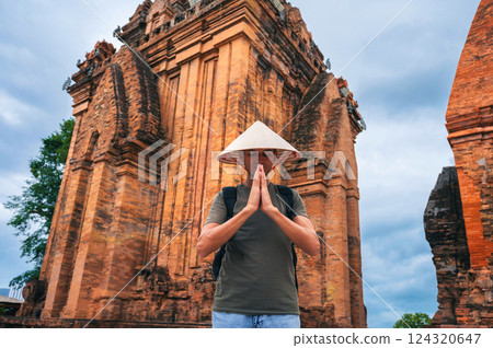 man in a Vietnamese cone hat non la prays at ancient Po Nagar Cham Towers in Nha Trang, Vietnam. The concept of travel in Asia man in a Vietnamese cone hat non la prays at ancient Po Nagar Cham Towers in Nha Trang, Vietnam. The concept of travel in Asia 124320647