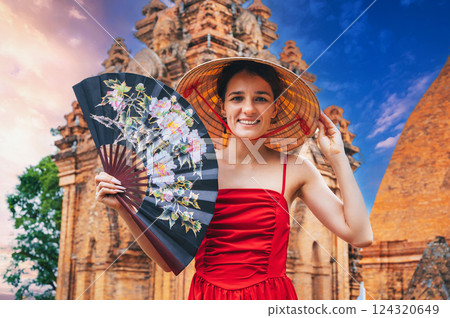 happy young woman tourist traveler in Vietnamese hat with a fan at Po Nagar Cham Towers in Nha Trang in Vietnam in Asia 124320649