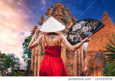 back of an Asian girl tourist traveler in a Vietnamese hat Non La with fan on Cham Towers of Po Nagar in Nha Trang in Vietnam in Asia 124320650