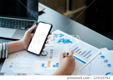 Businessperson using smartphone and laptop to analyze charts and graphs for data-driven decision-making in a modern office. Businessperson using smartphone and laptop to analyze charts and graphs for data-driven decision-making in a modern office. 124320763