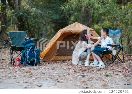 A mother and child share a moment at a campsite with a tent and chairs, surrounded by nature. A mother and child share a moment at a campsite with a tent and chairs, surrounded by nature. 124320791