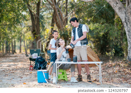 A happy family camping in the forest, setting up a picnic table and enjoying nature together on a sunny day. A happy family camping in the forest, setting up a picnic table and enjoying nature together on a sunny day. 124320797