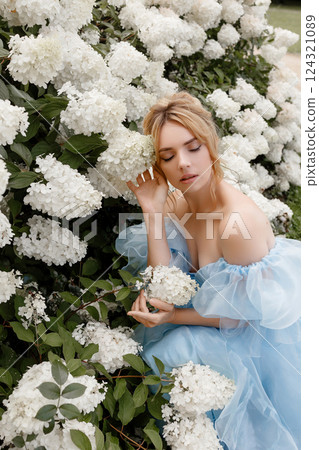 Woman in light blue ball gown poses near white lilacs Woman in light blue ball gown poses near white lilacs 124321089