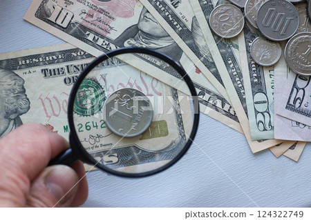 A hand holds a magnifying glass over one Russian ruble, over US dollars. A hand holds a magnifying glass over one Russian ruble, over US dollars. 124322749