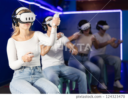 In darkened hall of gaming club, girl in VR helmet takes part in group game 124323470