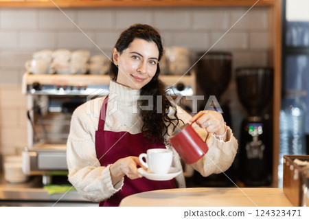 Girl cafe worker pours coffee from cezve coffee pot into cup Girl cafe worker pours coffee from cezve coffee pot into cup 124323471