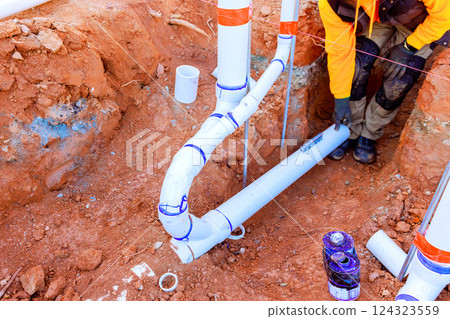 Worker is connecting PVC pipes in trench, ensuring proper alignment at construction location 124323559