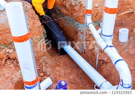 Contractor worker lays drainage pipes in trench at construction site, managing sewage water flow. 124323563