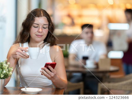 Girl in cafe drinks coffee and calling using mobile phone 124323666