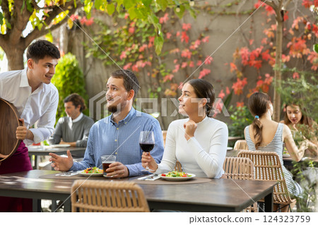 Waiter takes an order from a couple in love who decided to meet in an open air restaurant Waiter takes an order from a couple in love who decided to meet in an open air restaurant 124323759