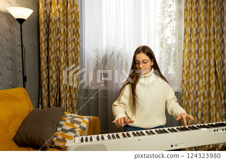 Young girl practicing piano in well-lit room with cozy decor. 124323980
