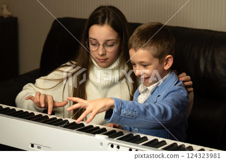 Young boy playing piano with teen girl mentor 124323981