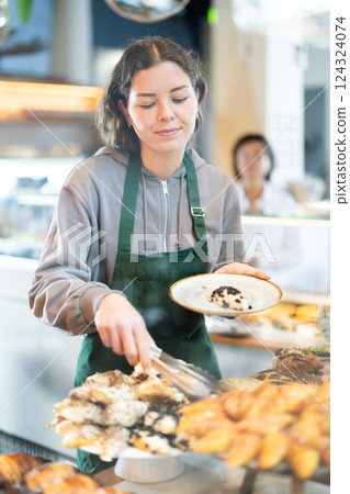 Young woman putting pastries on plate in cafe 124324074
