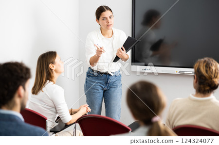 Young woman standing near interactive board and communicating with adult students during advanced training courses in classroom 124324077