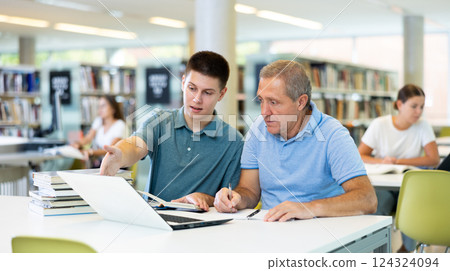 Concentrated males using laptop and talking with each other in the book space library Concentrated males using laptop and talking with each other in the book space library 124324094