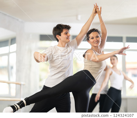 Young active man engaged in dance hall with female partner and practicing ballet arabesque pose during group class. Hobby lifestyle concept Young active man engaged in dance hall with female partner and practicing ballet arabesque pose during group class. Hobby lifestyle concept 124324107