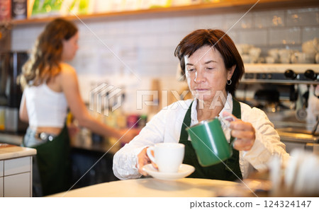 Senior woman cafe worker pours coffee from cezve coffee pot into cup 124324147
