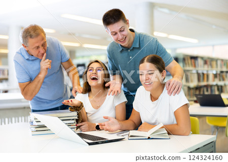 Mature librarian male bringing the index finger to the mouth to a group of laughing students in the library Mature librarian male bringing the index finger to the mouth to a group of laughing students in the library 124324160