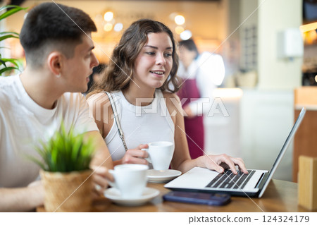 Man and woman sitting at table in cafe and looking at laptop 124324179