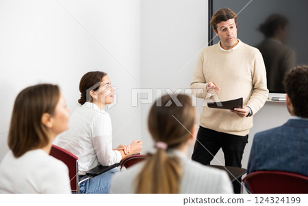 Friendly business coach answering questions from listeners sitting at desks at seminar in advanced training Friendly business coach answering questions from listeners sitting at desks at seminar in advanced training 124324199