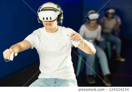 In darkened hall of gaming club, guy in VR helmet takes part in group game 124324234