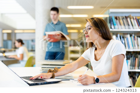 Portrait of adult latino woman studying at library using books and laptop Portrait of adult latino woman studying at library using books and laptop 124324313