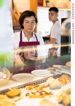 Mature woman seller laying out buns Mature woman seller laying out buns 124324314
