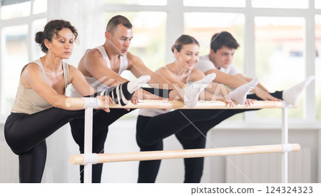 Female ballet student stretching at barre during group rehearsal 124324323