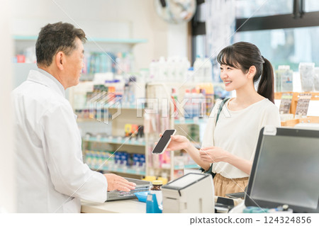 A woman who makes a smartphone payment at a pharmacy and a man who is a pharmacist/dispenser A woman who makes a smartphone payment at a pharmacy and a man who is a pharmacist/dispenser 124324856
