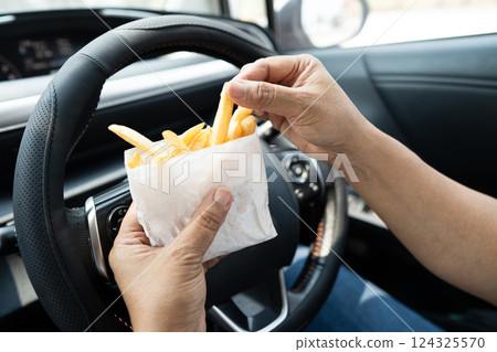 Asian lady holding French fries potato chips to eat in car, dangerous and risk an accident. 124325570