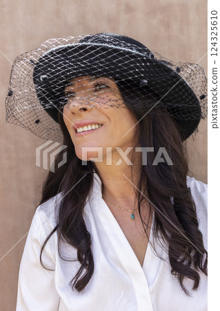 Smiling Lebanese Woman in Black Bucket Hats with Veil, Elegant Cloche Hat Wool Felt. Happy Elegant Female in her 50s with White Teeth Smile. Fashion, Style. Beige background. Vertical. Smiling Lebanese Woman in Black Bucket Hats with Veil, Elegant Cloche Hat Wool Felt. Happy Elegant Female in her 50s with White Teeth Smile. Fashion, Style. Beige background. Vertical. 124325610