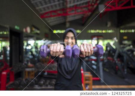 Arab middle eastern muslim woman working out while lifting a dumbbell at the gym. Fitness exercise and healthy lifestyle concept 124325725