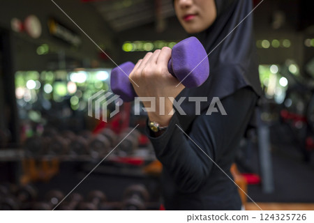 Arab middle eastern muslim woman working out while lifting a dumbbell at the gym. Fitness exercise and healthy lifestyle concept 124325726