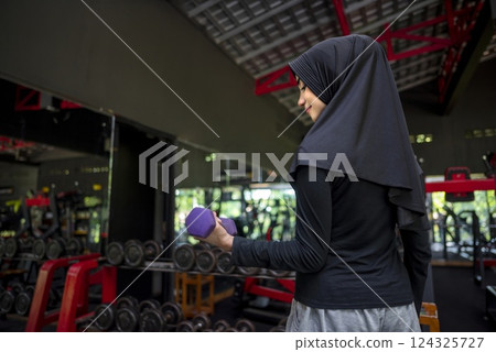 Arab middle eastern muslim woman working out while lifting a dumbbell at the gym. Fitness exercise and healthy lifestyle concept 124325727